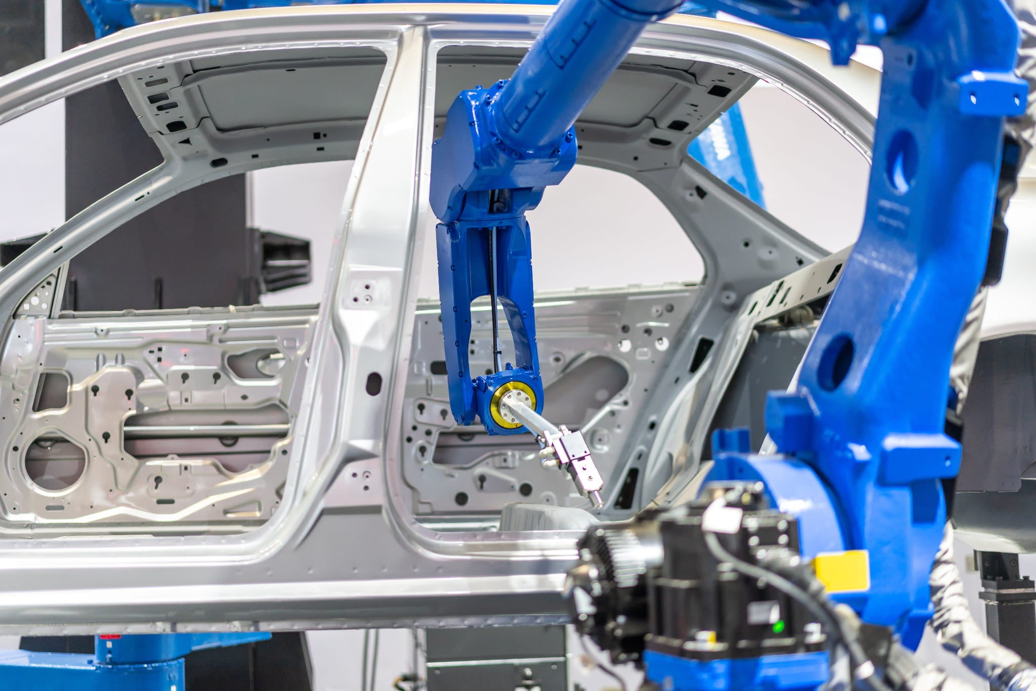 Automotive assembly line with a blue robot arm working on a car frame.