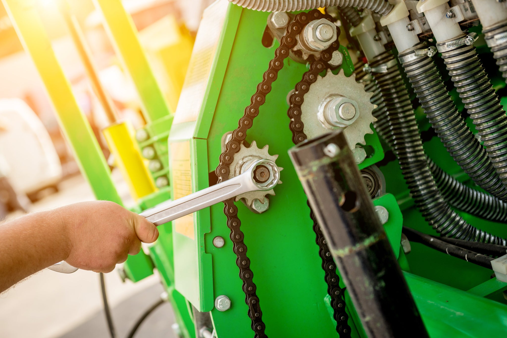 Person using a wrench on a green machine with gears and chains.